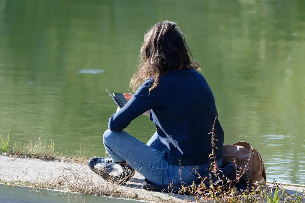Vacancière assise au bord d'un lac, son téléphone à la main